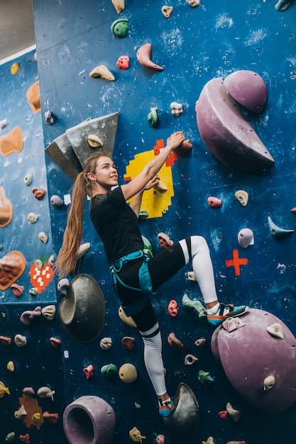 Young woman climbing a tall, indoor, man-made rock climbing wall