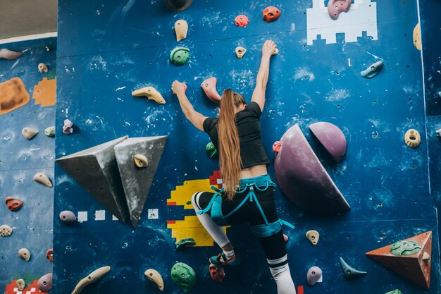 Young woman climbing a tall, indoor, man-made rock climbing wall