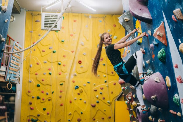 Young woman climbing a tall, indoor, man-made rock climbing wall