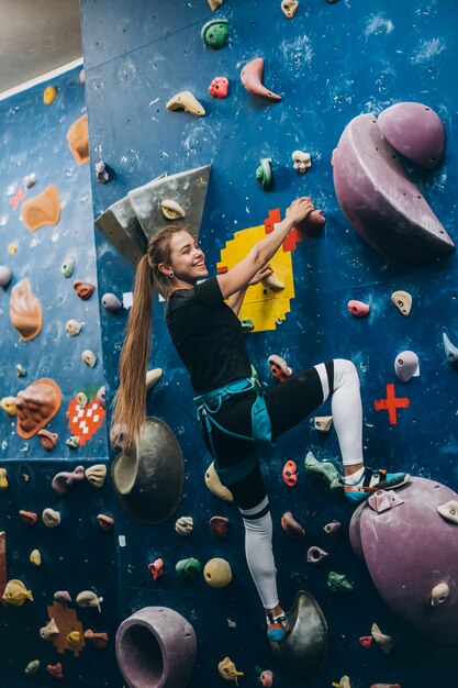 Young woman climbing a tall, indoor, man-made rock climbing wall