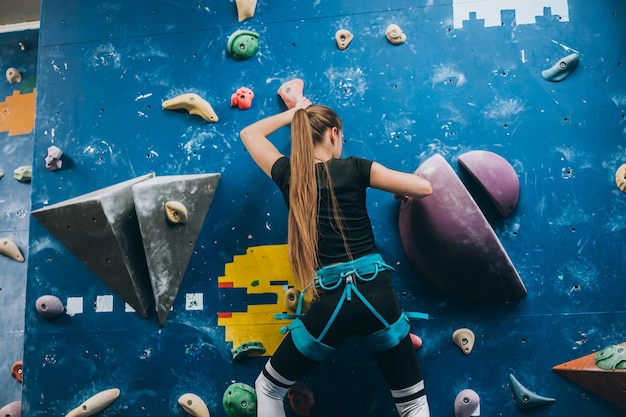 Young woman climbing a tall, indoor, man-made rock climbing wall