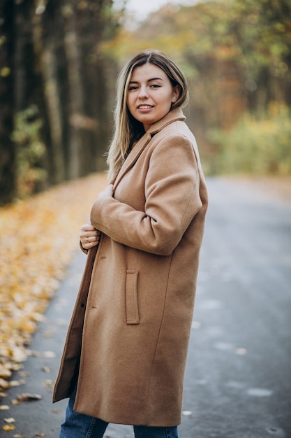 Free photo young woman in coat standing on the road in an autumn park