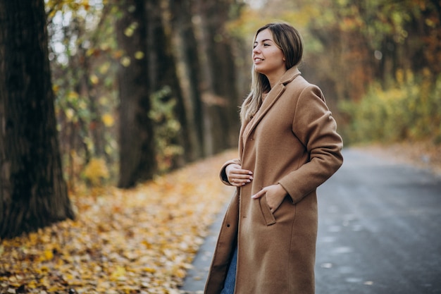 Free photo young woman in coat standing on the road in an autumn park