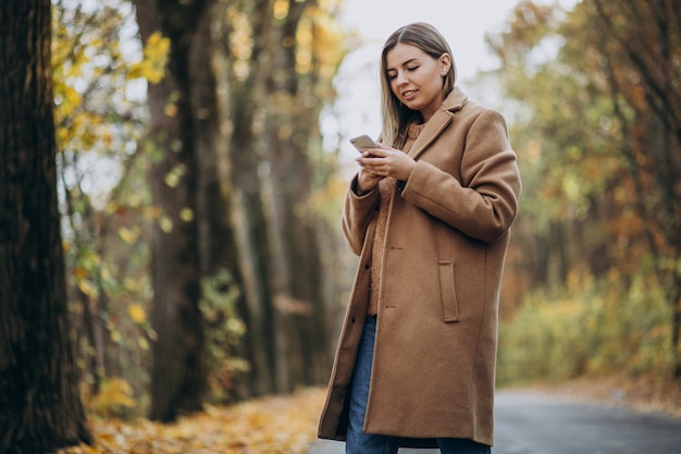 Young woman in coat standing on the road in an autumn park