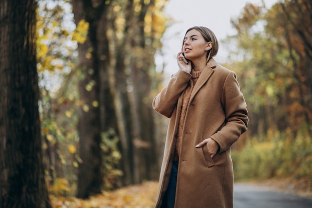 Free photo young woman in coat standing on the road in an autumn park