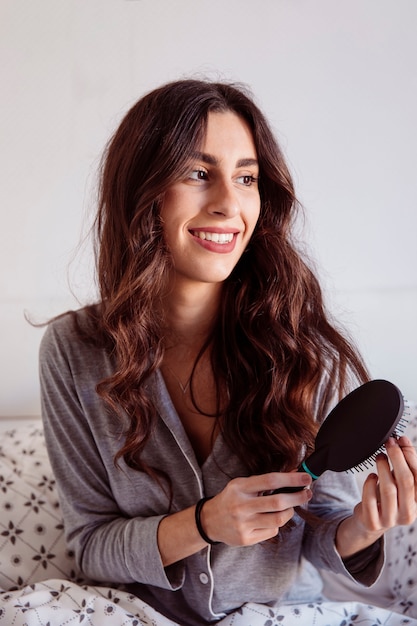 Young woman combing hair in bed