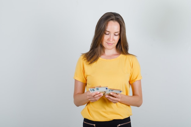 Young woman counting money in yellow t-shirt, black pants and looking careful