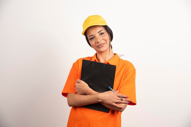 Young woman courier holding clipboard on white wall.