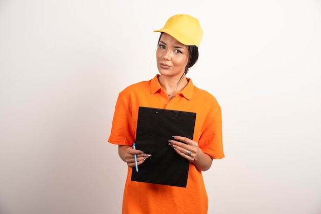 Young woman courier holding clipboard on white wall.