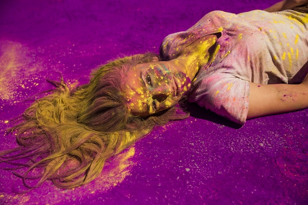 Free photo young woman covered with powder lying on purple holi color