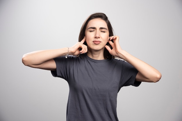 Young woman covering her ears over a gray background