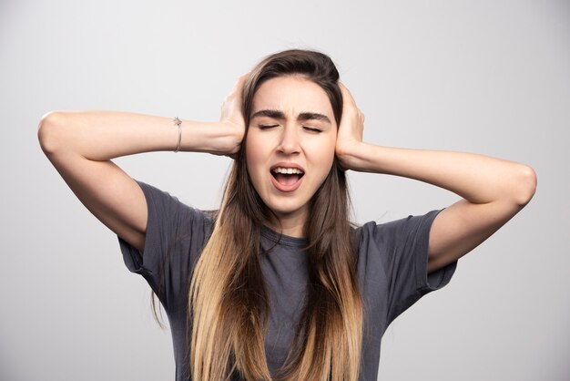 Young woman covering her ears with hands over a gray background.