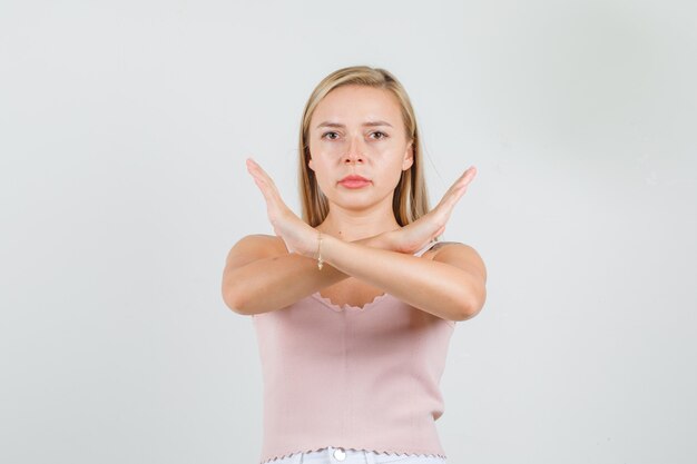 Young woman crossing arms doing negative sign in singlet, mini skirt and looking serious