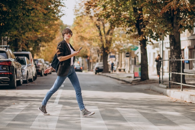 Free photo young woman crossing road and using phone