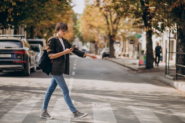 Free photo young woman crossing road and using phone