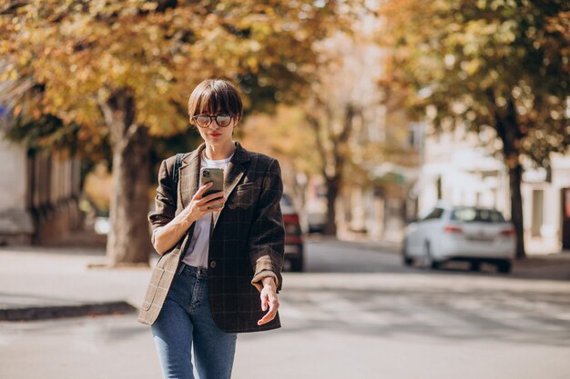 Young woman crossing road and using phone