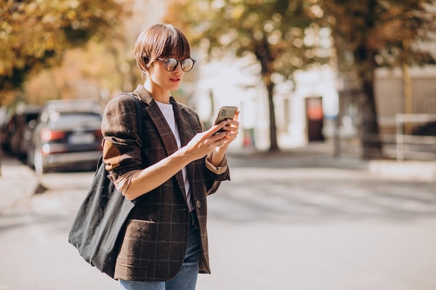 Young woman crossing road and using phone