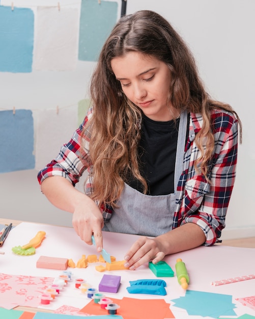 Young woman cutting clay using clay cutter on desk