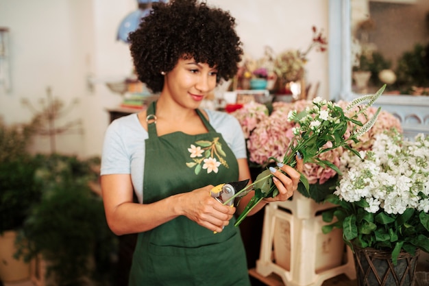 Young woman cutting stem of flowers with secateurs in flower shop