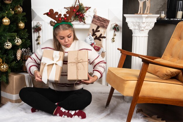 A young woman in deer ears looking at two Christmas presents.