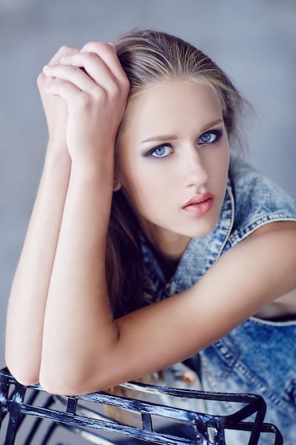 Free photo a young woman in denim jacket and black pants posing near concrete wall.