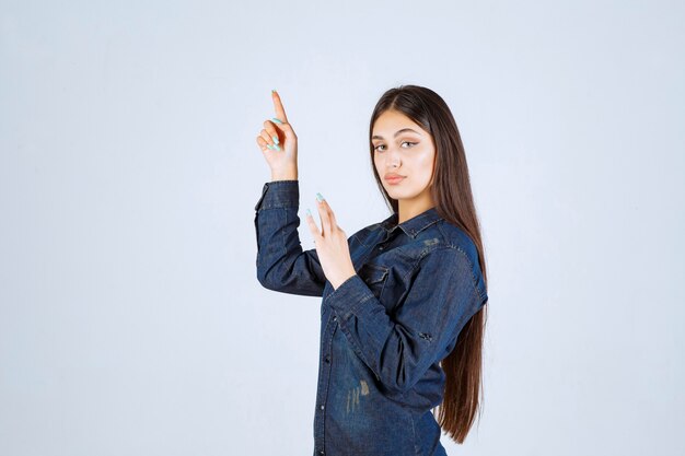 Young woman in denim shirt raising her hands up and pointing at something above