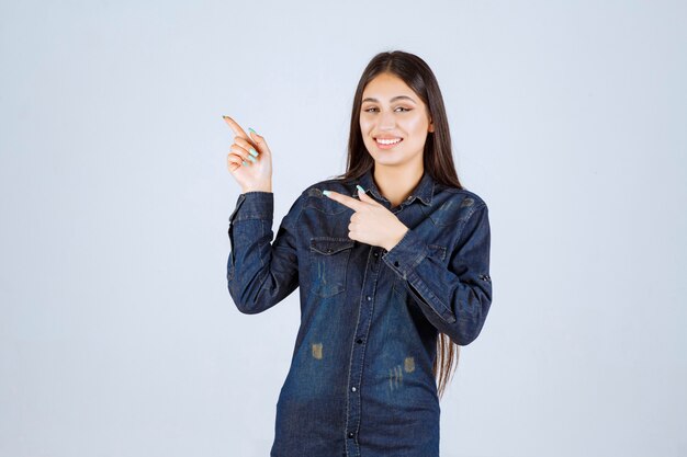 Young woman in denim shirt raising her hands up and pointing at something above