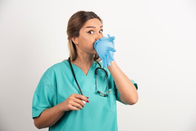 Young woman doctor wearing latex gloves and scrubs on white background.