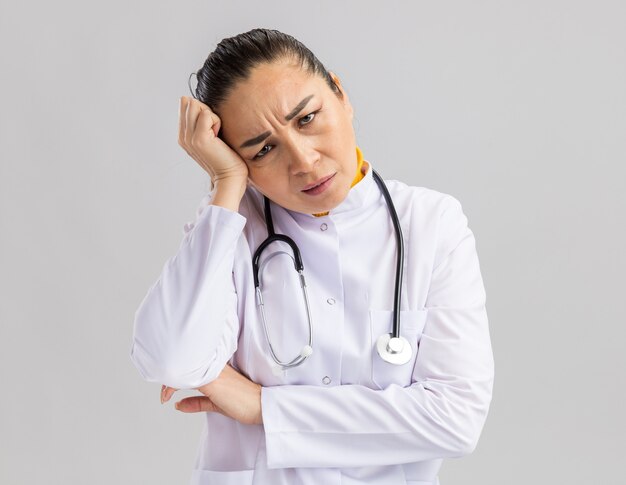 Young woman doctor in white medical coat with stethoscope around neck   being annoyed and irritated