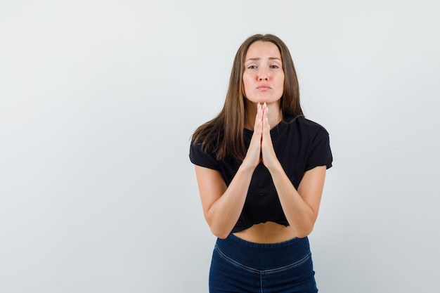 Young woman doing pray gesture in black blouse and looking sad.