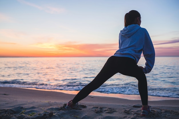 Young woman doing sport exercises on sunrise beach in morning