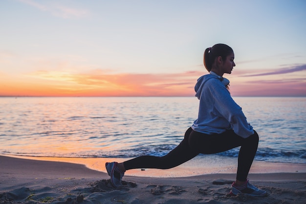 Young woman doing sport exercises on sunrise beach in morning