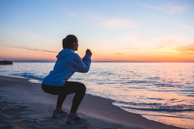 Young woman doing sport exercises on sunrise beach in morning