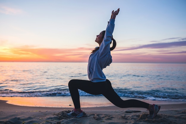 Young woman doing sport exercises on sunrise beach in morning