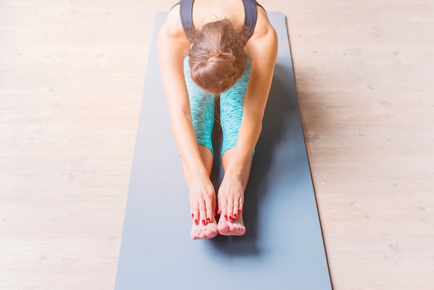 Free photo young woman doing stretching exercise on yoga mat