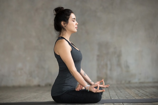 Young woman doing Sukhasana exercise, side view