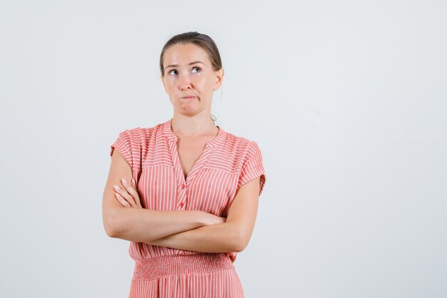 Young woman in dress looking up with crossed arms and looking pensive , front view.