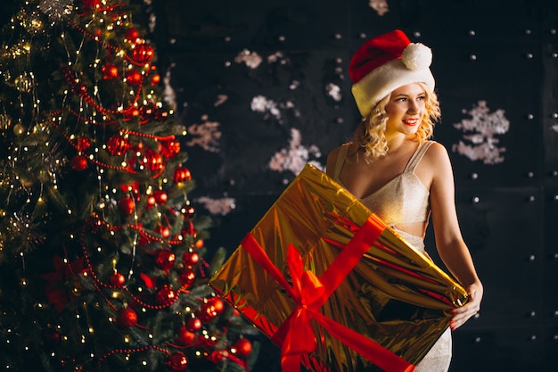 Free photo young woman in dress with christmas presents by christmas tree