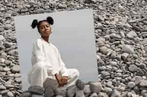 Free photo young woman dressed in white posing with mirror in rocks