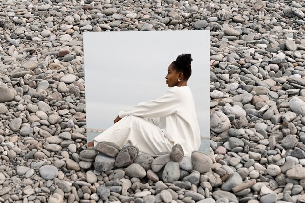 Young woman dressed in white posing with mirror in rocks