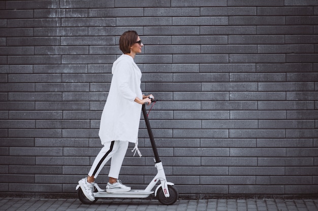 Young woman dressed in white riding scooter