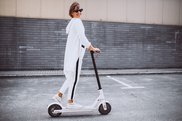 Young woman dressed in white riding scooter