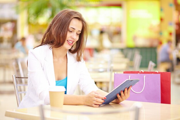 Young woman drinking coffee and consulting tablet