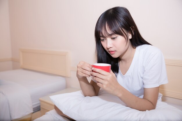 Young woman drinking coffee at home in her bed and checking her laptop