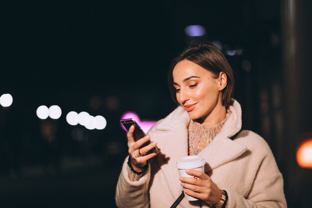 Young woman drinking coffee at night street