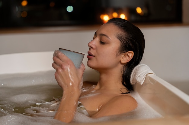 Young woman drinking coffee and relaxing while taking a bath