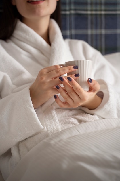 Free Photo young woman drinking coffee while sitting on the bed in a hotel room