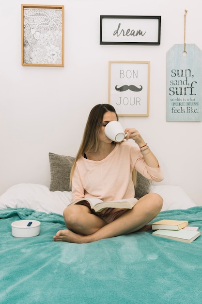 Young woman drinking and reading on bed