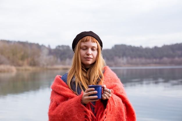 Young woman drinks coffee cup on lake shore