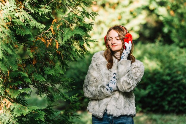 Young woman in earmuffs near coniferous twigs